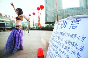 11月26日下午，在市府廣場(chǎng)，一位“舞娘”在人群中跳起了肚皮舞。然而，如果不看“她”寫在木板上的求助信，誰也難以看出，眼前這位舞姿翩翩的嬌媚舞娘，其實(shí)是男兒身。